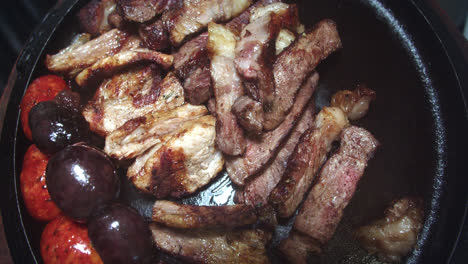 beautiful slow motion shot of chunks of meat being placed on a grill plate with sausages, sliced loin and potatoes inside a restaurant kitchen