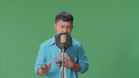 young asian boy singing into microphone in green screen studio