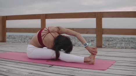 woman practicing yoga on a wooden deck by the beach