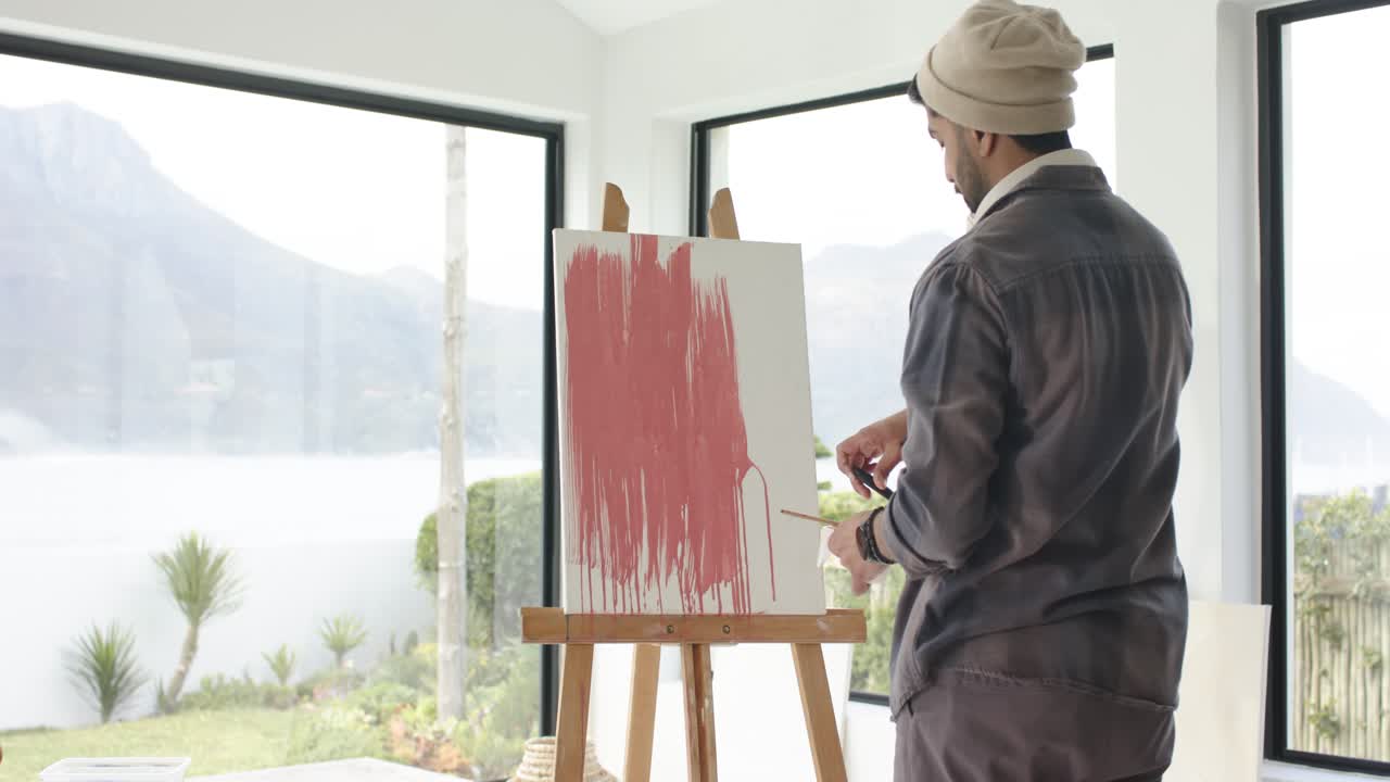 Indian painter scooping red paint, painting strokes, adding lines on canvas in studio, copy space