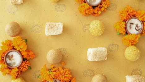 tilt across indian sweets, flowers, diyas on a indian background for hindu festival of lights, dusshera and diwali preparation and celebration ingredients