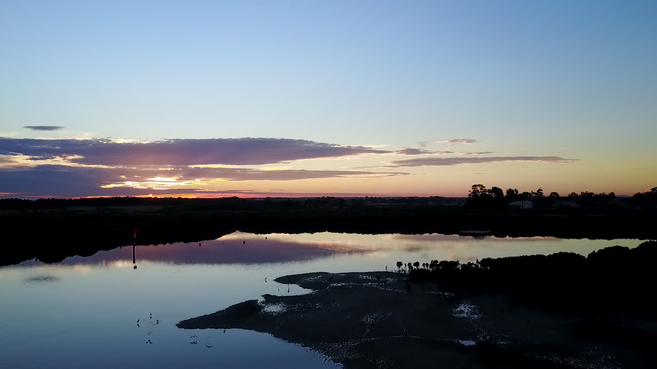 태양을 향해 낮은 고도에서 잔잔한 물 위에 드론이 있는 일몰 항공 영상