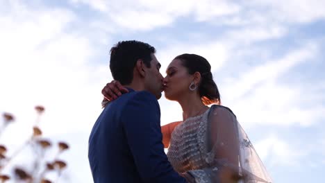 indian hindu groom and bride kissing against cloudy blue sky - low angle shot