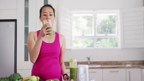 relaxed asian woman drinking smoothie in kitchen