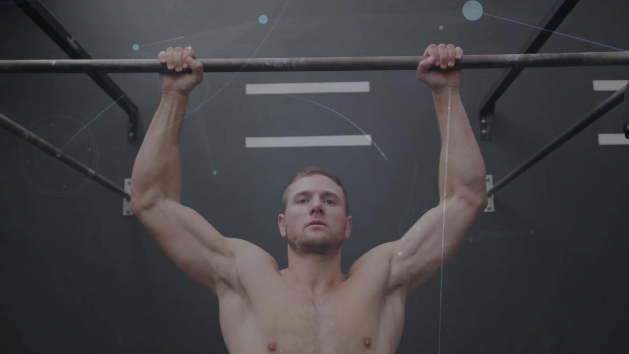 Segurando a barra, homem sem camisa fazendo flexões em aparelho de ginástica, reflexos de luz mostrando marcas na parede