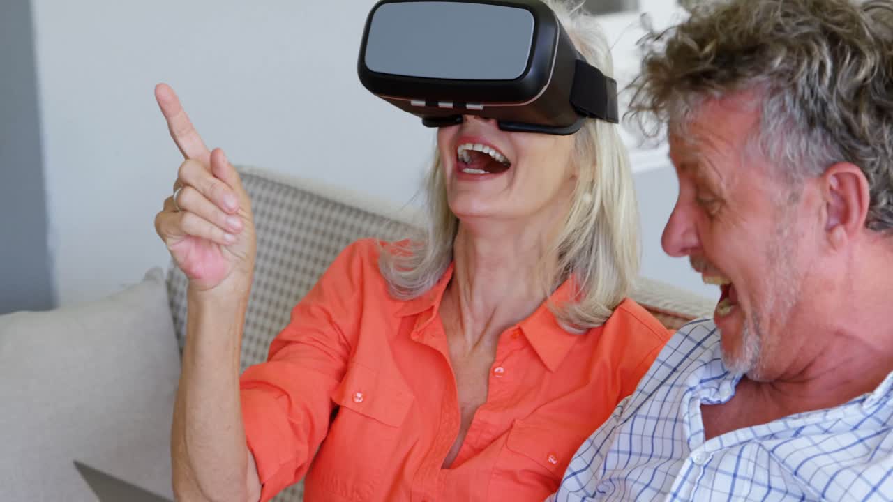 Coppia di anziani che usa laptop e visore VR sul divano 4k