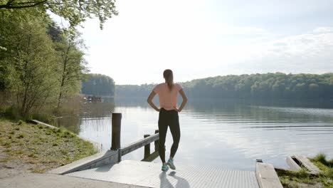 Woman-standing-by-shore-of-lake-looking-into-water-on-sunny-day