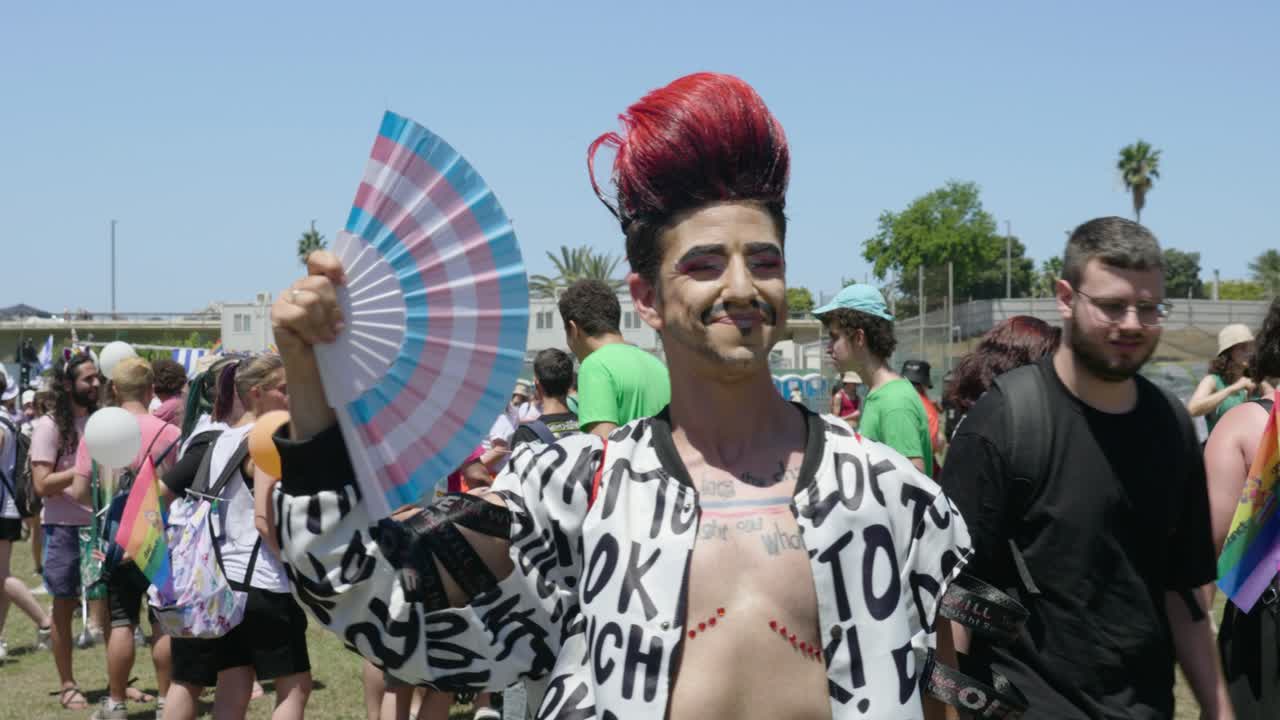 A large crowd had gathered in a garden by the side of the road. Standing there, a boy is blowing wind with a colorful blower and making various gestures