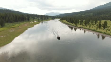 Aerial-footage-following-in-front-of-a-boat-going-down-a-river-in-the-mountains-and-forests-in-a-beautiful-remote-setting