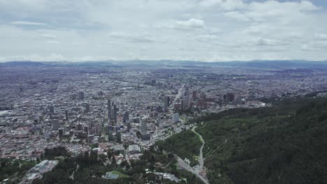 aerial view from the lush green mountain top to the vast city of bogotá, with a close-up in direction to the clouds filling the sky.