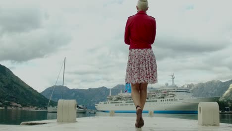 mujer caminando en un muelle con un crucero en el fondo