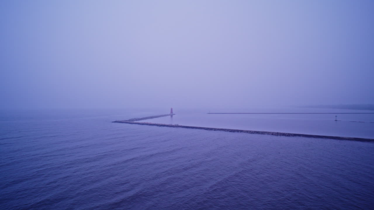 Drone shot flying away from lighthouse on the end of a breakwater in lake Michigan