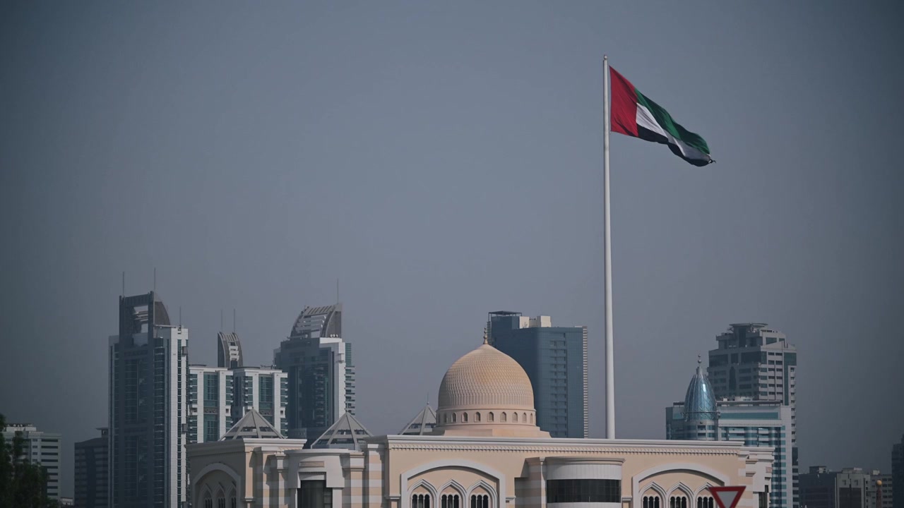 United Arab Emirates flag waving above the urban landscape of Sharjah