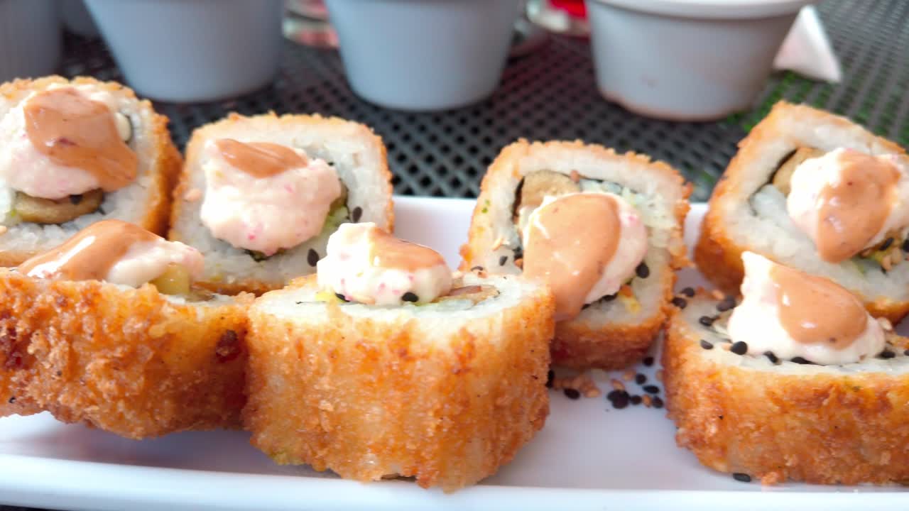 Side view of crispy fried sushi rolls with creamy sauce on top, served on a white plate with sesame seeds.