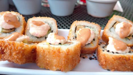 side view of crispy fried sushi rolls with creamy sauce on top, served on a white plate with sesame seeds.