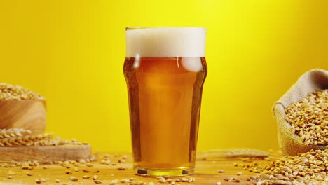 glass of beer on wooden table with barley grains