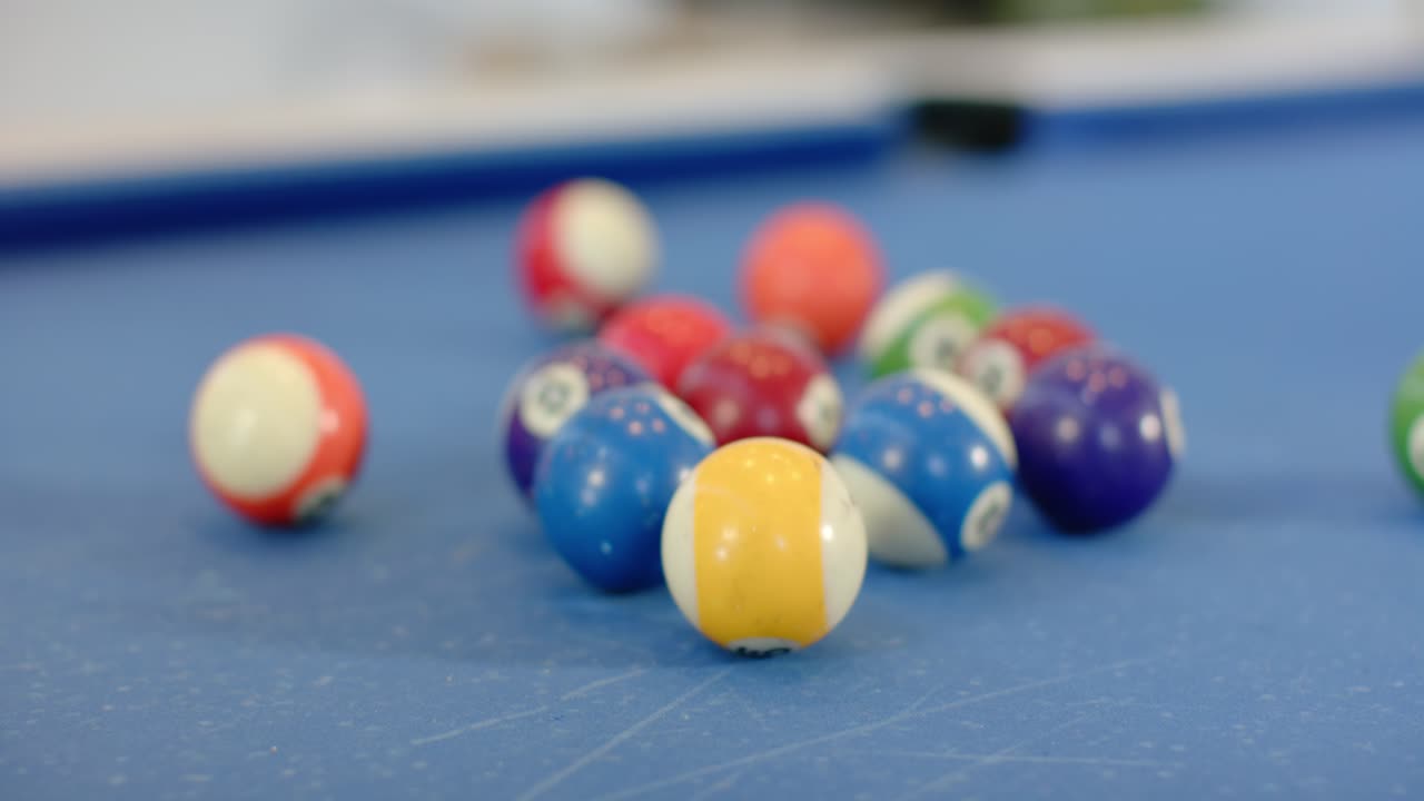 Numbered pool balls are scattering on blue-felt table after unseen cue ball breaks rack