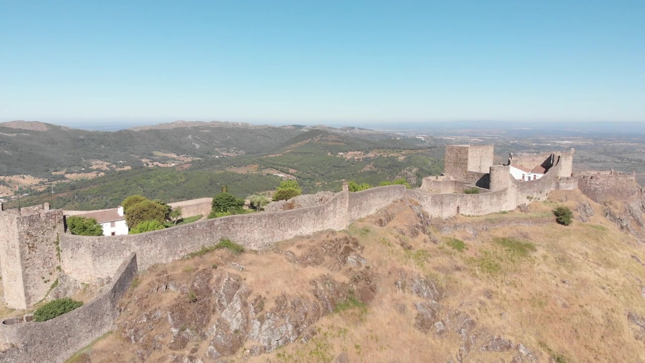 Avvicinamento aereo con drone verso il castello di Marvão da un'inquadratura ampia e distante, che rivela la fortezza e il paesaggio portoghese circostante