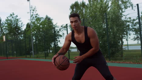 Focused-sporty-mixed-race-player-practicing-street-basketball-outdoor.