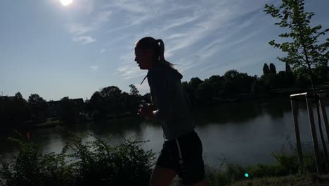 silueta de una joven rubia corriendo alrededor del lago en un día soleado