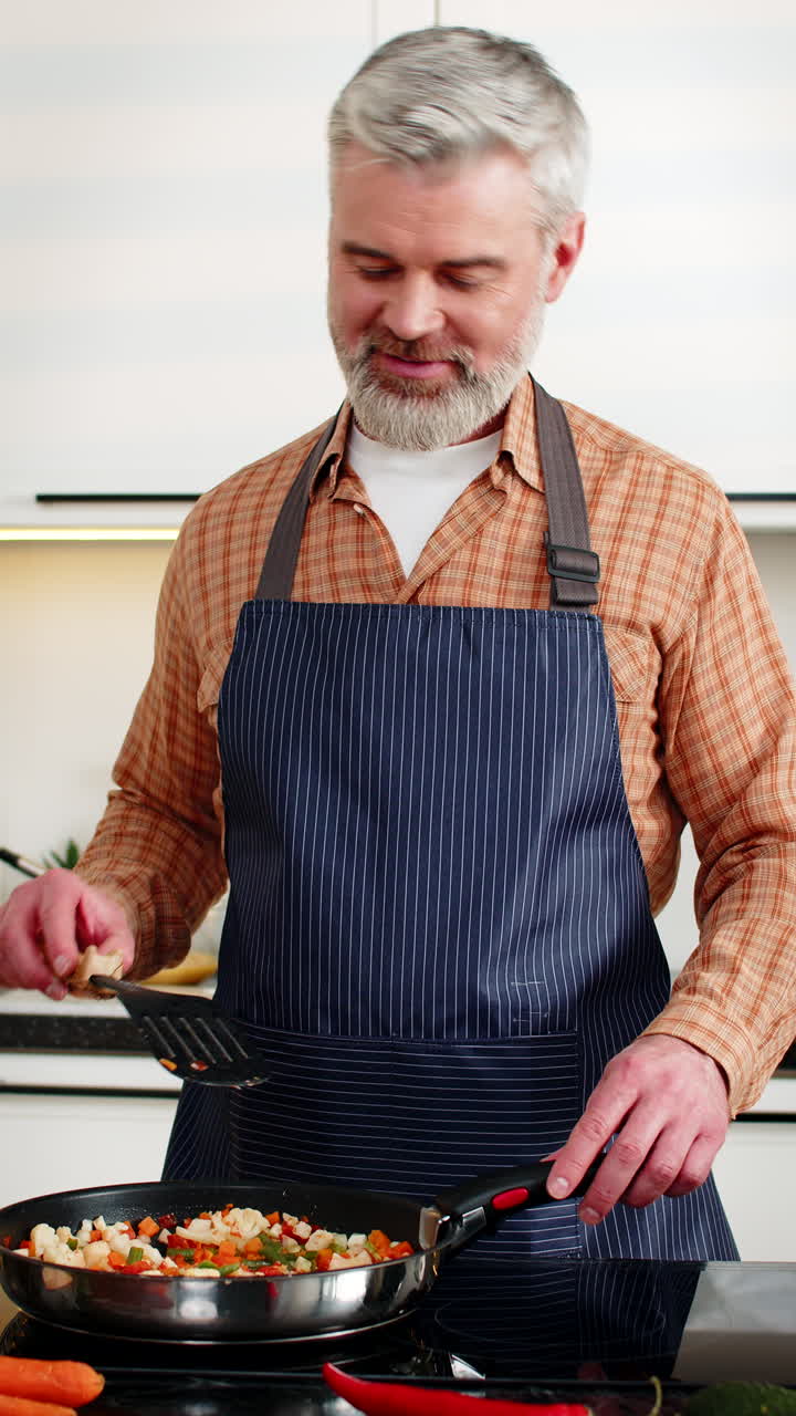 Uomo di mezza età che cucina verdure salutari su fornello elettrico nella cucina di casa per un piano alimentare dietetico