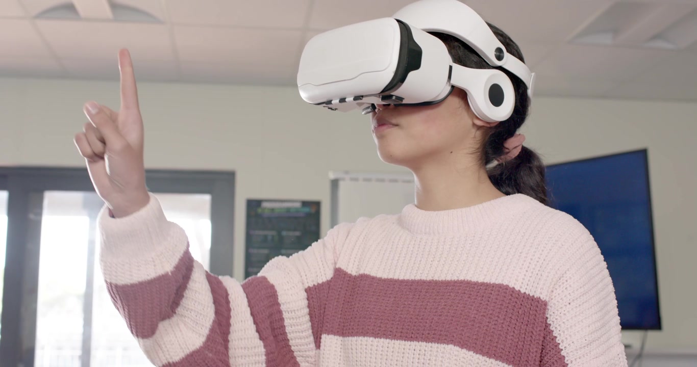 Giovane afroamericano che usa un visore VR e gesticola in laboratorio, mentre i coetanei guardano dai laptop