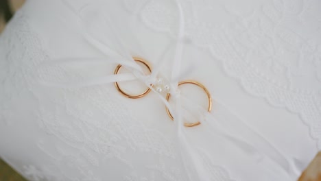 a pair of golden wedding rings tied with a white ribbon on a laced pillow