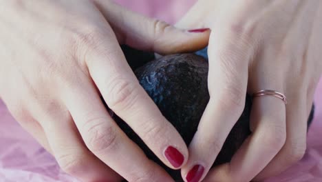 tres aguacates se colocan sobre una tela rosa, dos manos de niña entran y toman una muy suavemente, escena en cámara lenta y luz natural