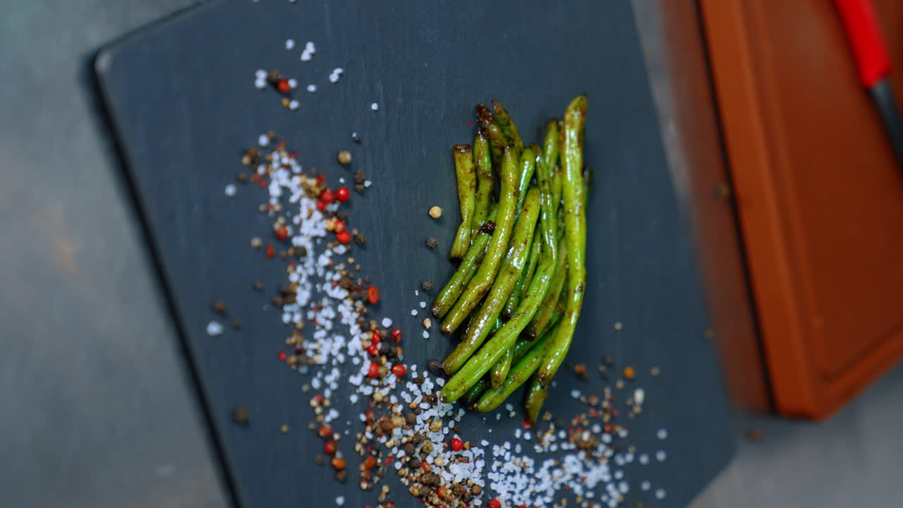 Fried green beans are put on the black charcuterie board. The plate is decorated with salt and pepper. Close up. Vertical view.