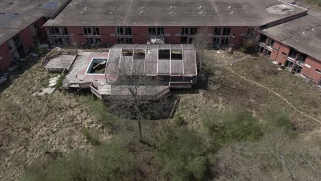 aerial drone footage panning up while backing away from a creepy abandoned hotel and covered pool