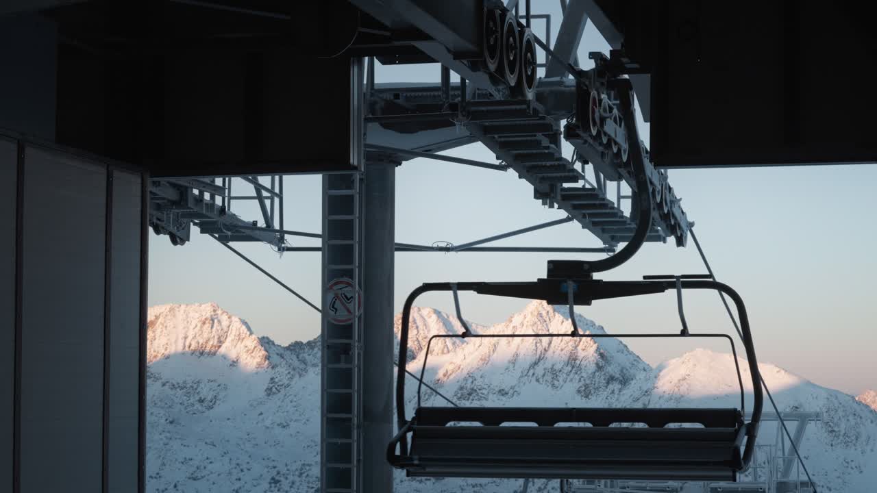 Detailed shot of ski lift machinery with cables and pulleys, snowy sunlit mountains in the background. Andorra