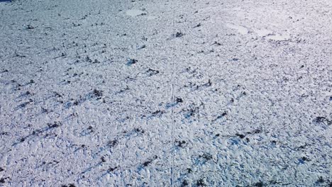 Revealing-aerial-view-of-snowy-bog-landscape-with-hiking-trail-and-frozen-lakes-in-sunny-winter-day,-Dunika-peat-bog-,-high-altitude-wide-angle-drone-shot-moving-forward,-tilt-up