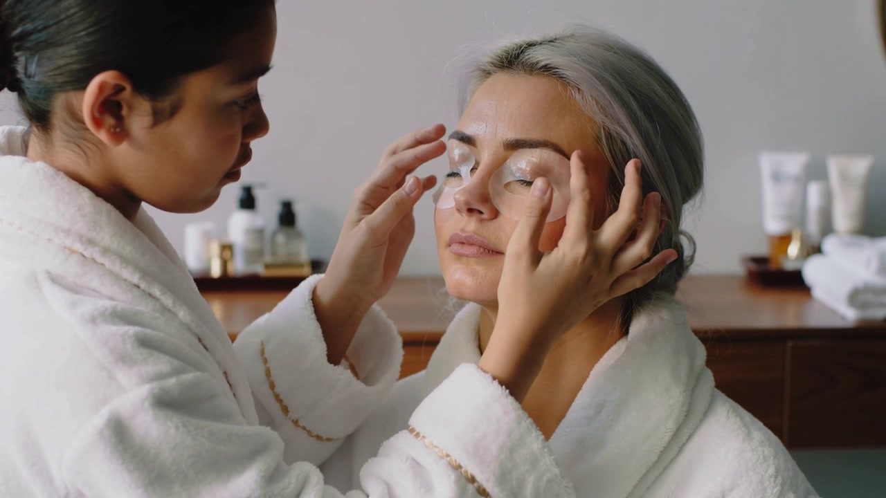 Therapeutin im Bademantel bringt Augenpads und legt sie einem Kunden im Spa-Raum zur Hydration auf.