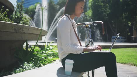 african american woman with bike using laptop in city park