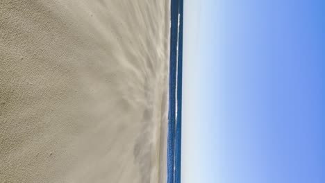 beach sand being blown up by the wind, summer breeze, vertical video of a dreamy bright blue sky beachy friendly sandstorm