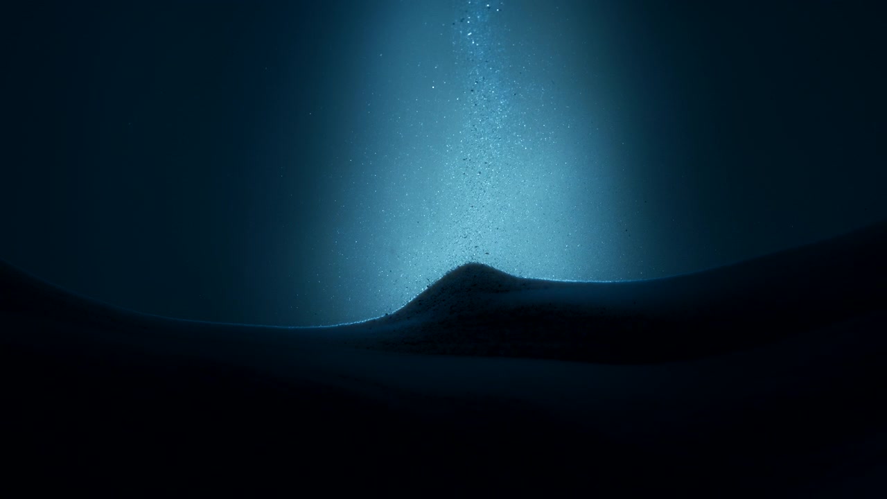 Luz azul incidindo sobre partículas de areia caindo na pilha de areia em câmera lenta