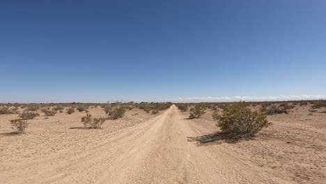 driver point of view driving along a dirt road in the barren mojave desert's arid landscape