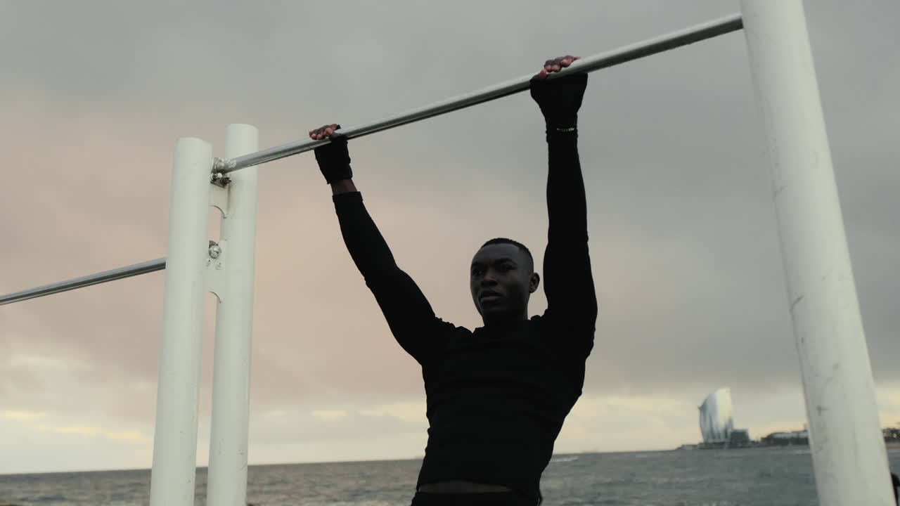 Young Black Man Hanging on Pull-Up Bar at Urban Beach