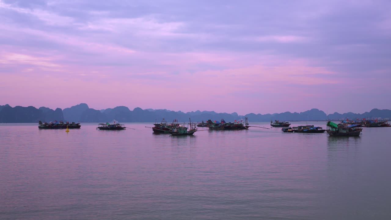 Ha Long Bay traditional fishing trawlers float serenely against the backdrop of limestone karsts during a purple-hued sunset in Vietnam
