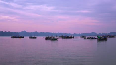 ha long bay traditional fishing trawlers float serenely against the backdrop of limestone karsts during a purple-hued sunset in vietnam