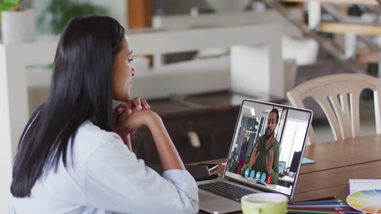Mixed race businesswoman sitting at table using laptop having video call with male colleague