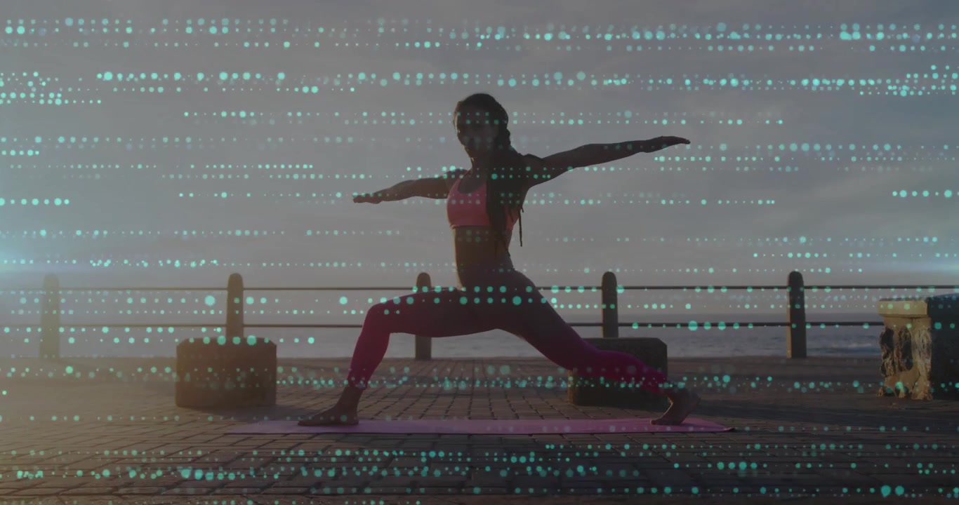 Woman placing pink yoga mat on oceanfront and flowing into warrior II during stretch at sunrise