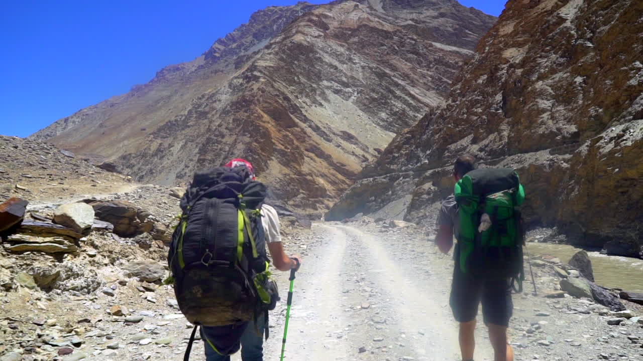 POV shot as walking between hikers, people with backpacks on a dusty road on a hot summer day in the eHimalayas.