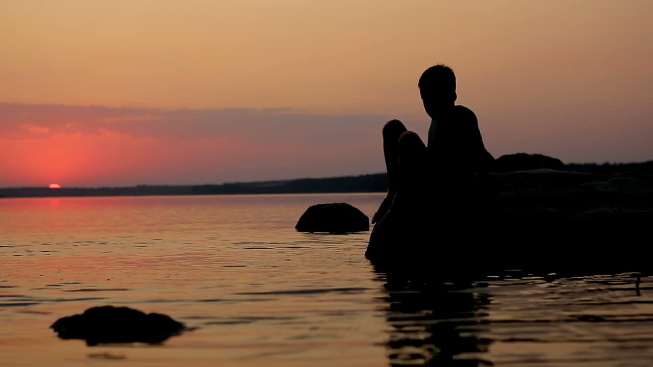 Boy Playing On Stone. Young child playing on stone near water at sunset