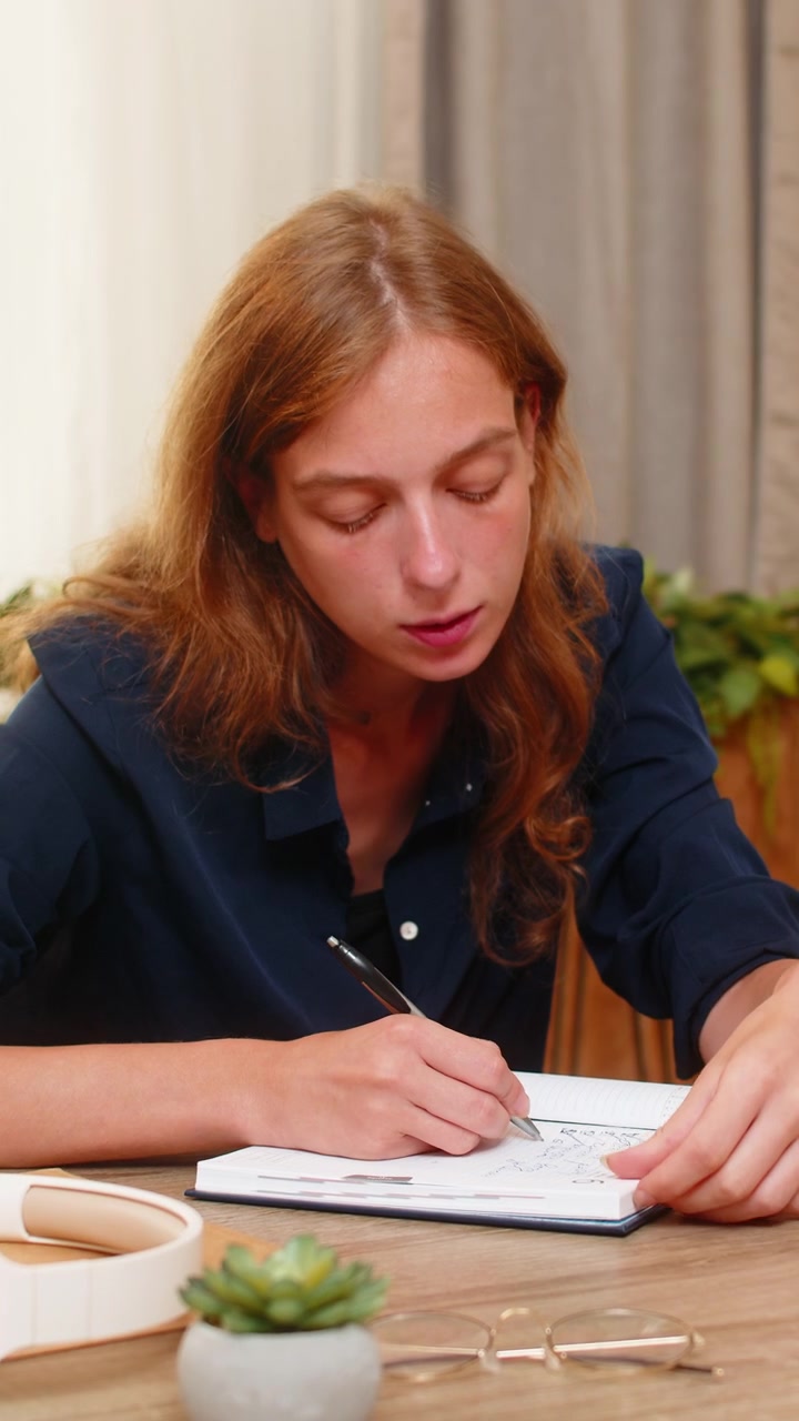 Giovane donna al tavolo di casa che riflette con un quaderno e annota idee per i futuri piani delle attività quotidiane.