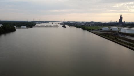 Aerial-dolly-forward-shot-over-a-river-with-the-sun-low-on-the-horizon-and-silhouettes-of-industrial-towers-and-bridges-are-visible