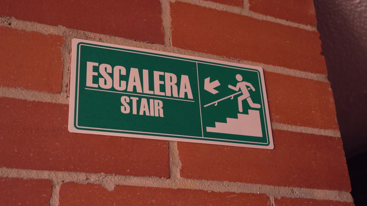 Green and white bilingual sign in spanish and english indicating stairs on a red brick wall
