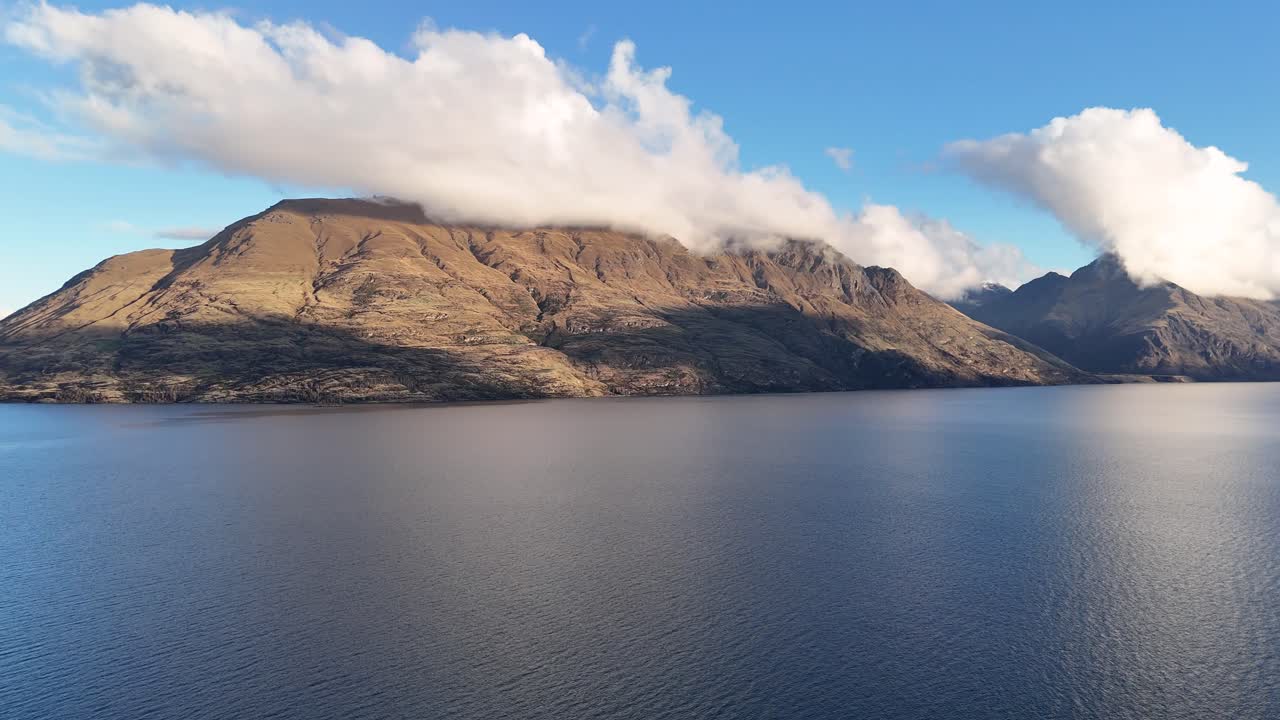 A tranquil scene of a mountain and lake under a clear blue sky with soft clouds