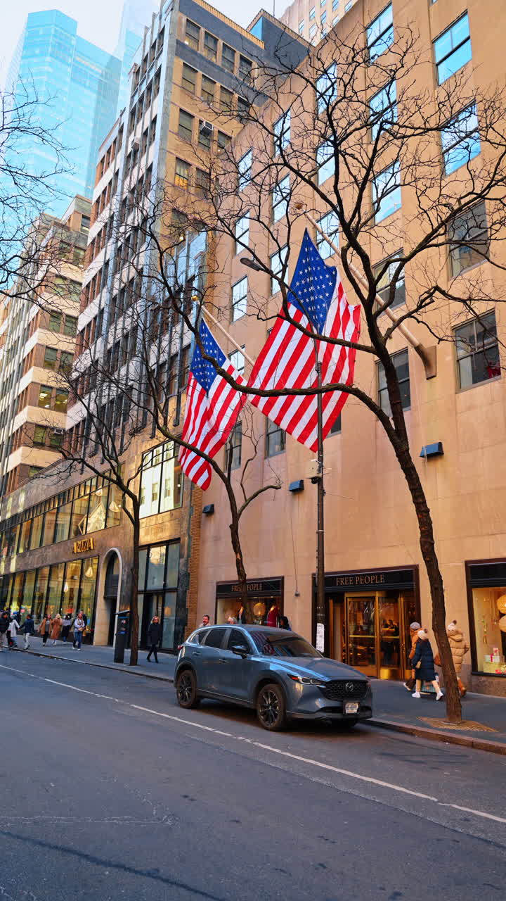 New York, USA, 18 dicembre 2025: Facciate di grattacieli decorate con bandiere americane. Persone con abiti caldi camminano per le strade di New York, USA. Video verticale.