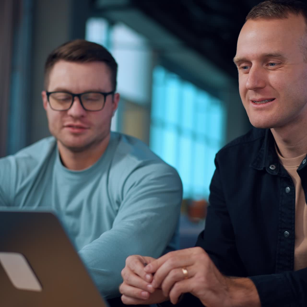 Two young men sitting indoors in front of laptop. Businessmen discussing work, communicating or brainstorming using computer